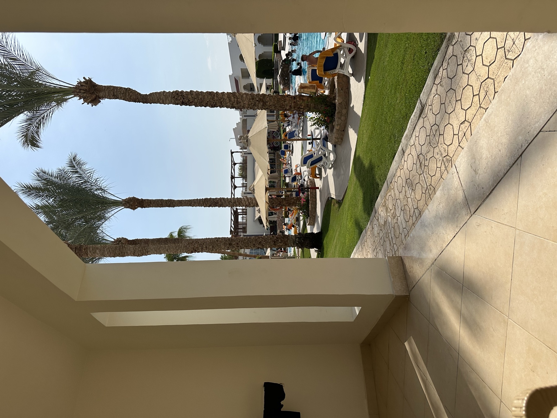 Blick durch einen schattigen Durchgang auf Palmen und einen Resortgarten in Ägypten